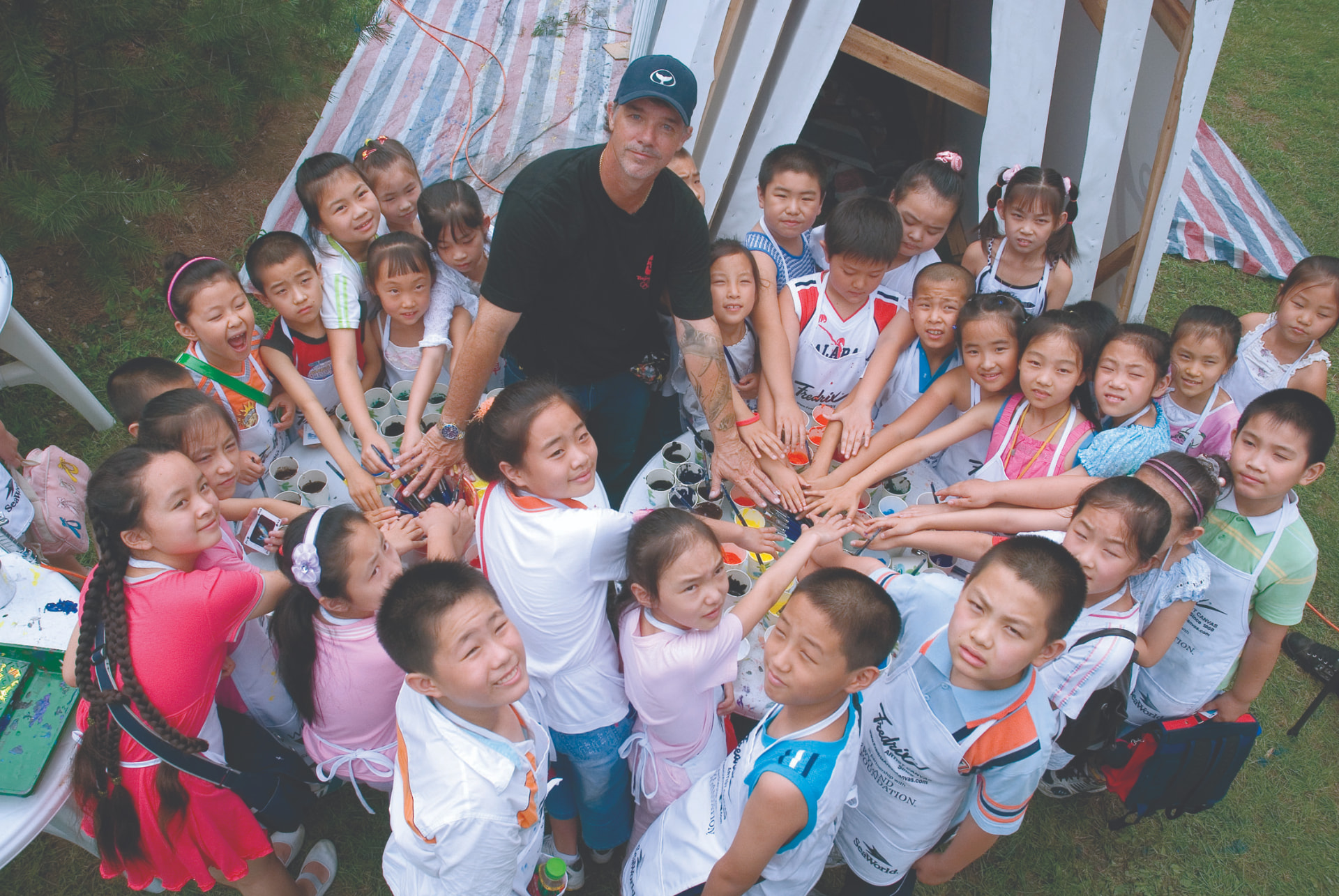 Wyland painting with a circle of children during a community outreach event