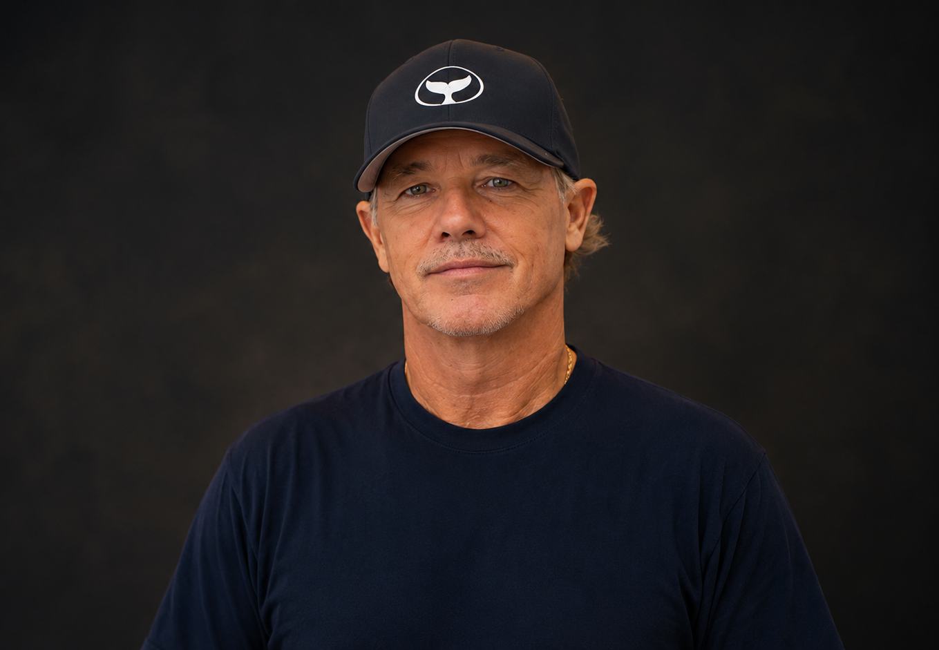 Portrait of the marine life artist Wyland wearing a whale-tail cap against a dark backdrop